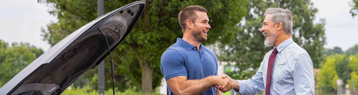 Two men shaking hands next to car with hood open