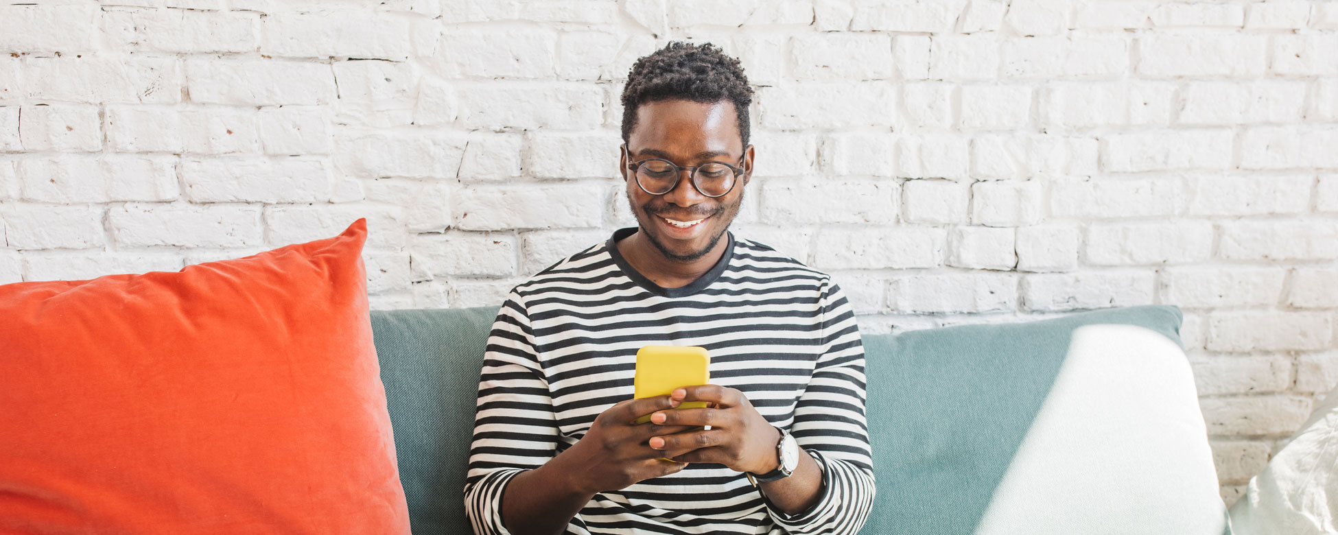 Young and cheerful man sitting on sofa and looking at phone