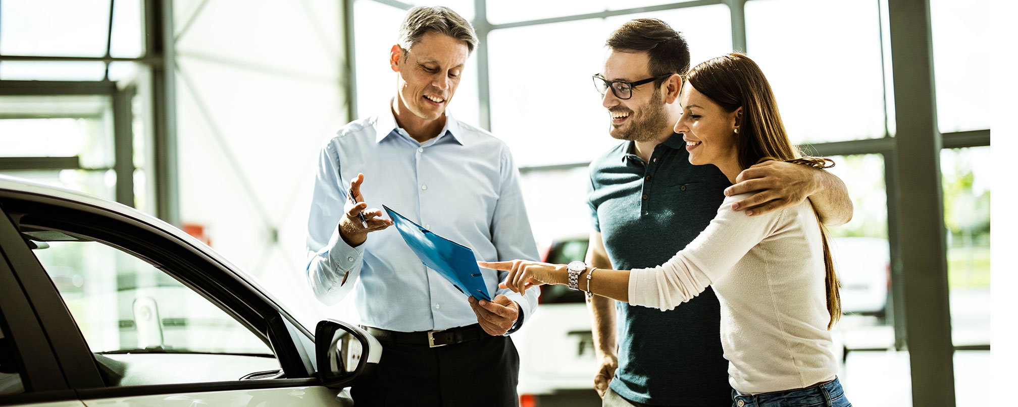 couple speaking with salesman at car dealership