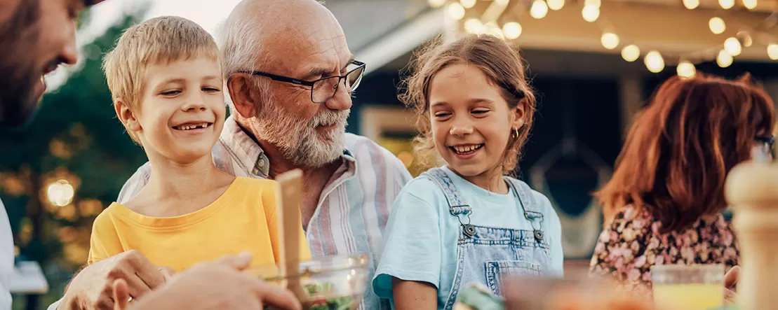 grandfather holding grandkids outside during summer bbq