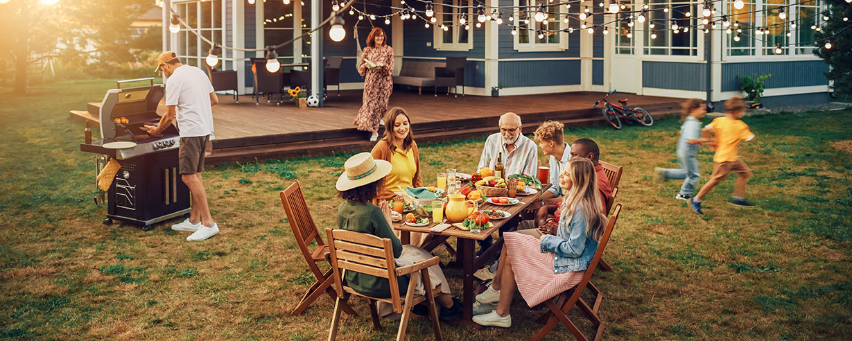 family and friends gathered in a yard at sunset having a bbq
