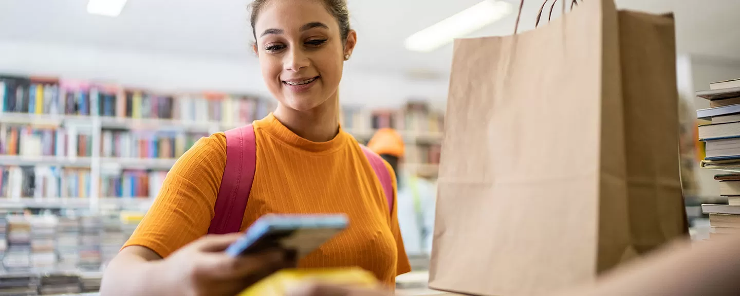 Female high school or college student buying books with her phone using tap to pay