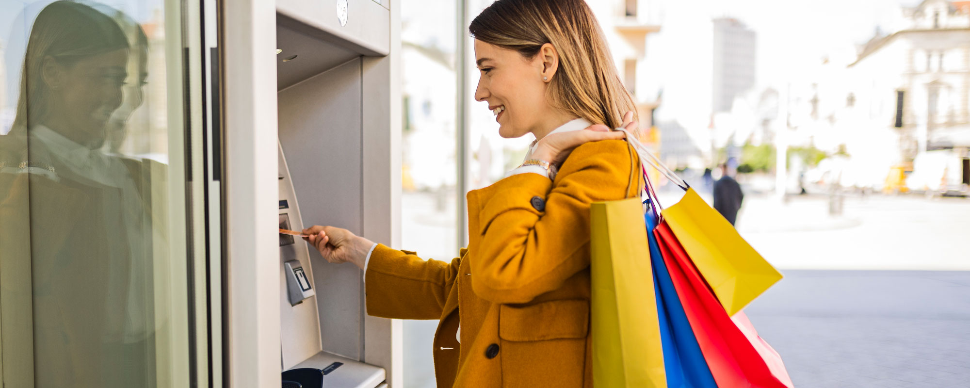 Young woman with shopping bags taking using the ATM