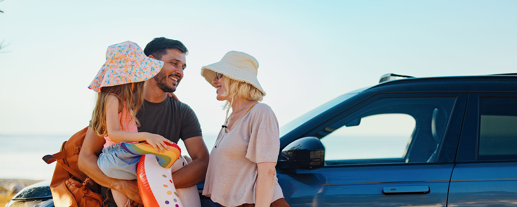 Husband, wife and daughter standing outside car smiling