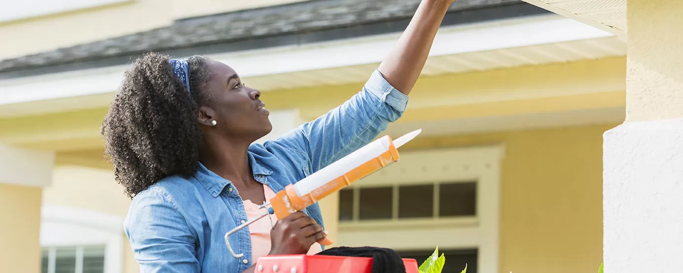 Woman installing caulk on home gutters