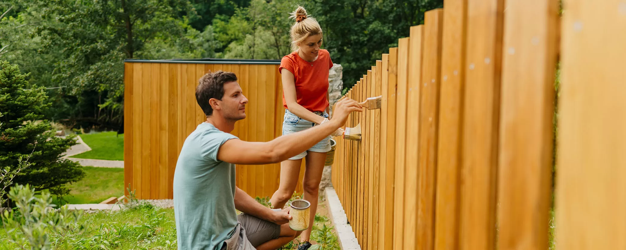 Man and woman staining wood fence outdoors