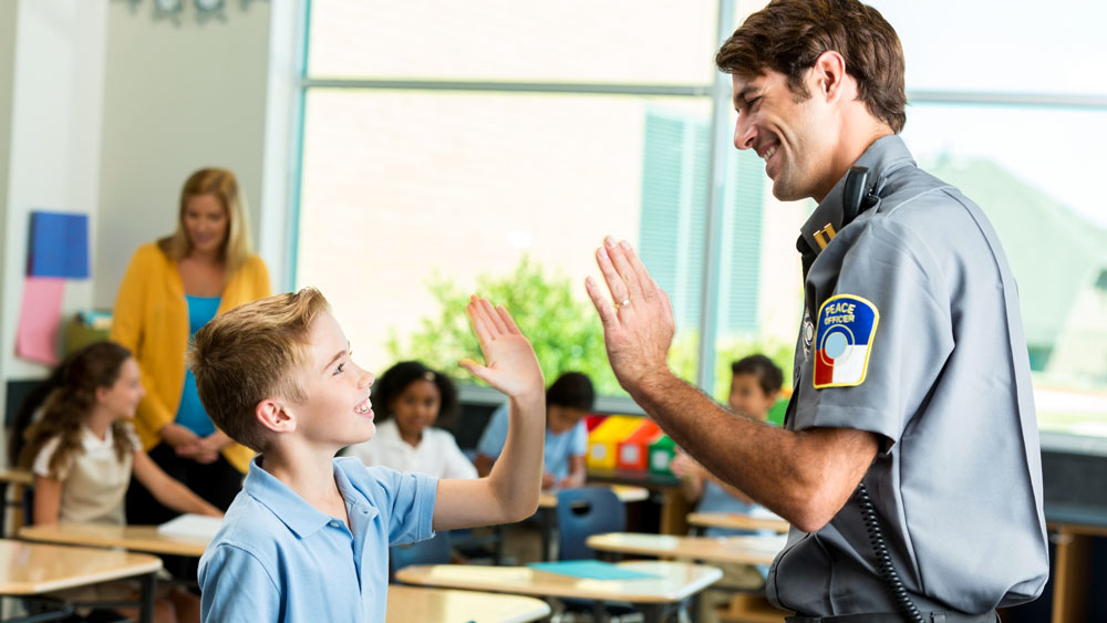 Happy police officer gives high five to student