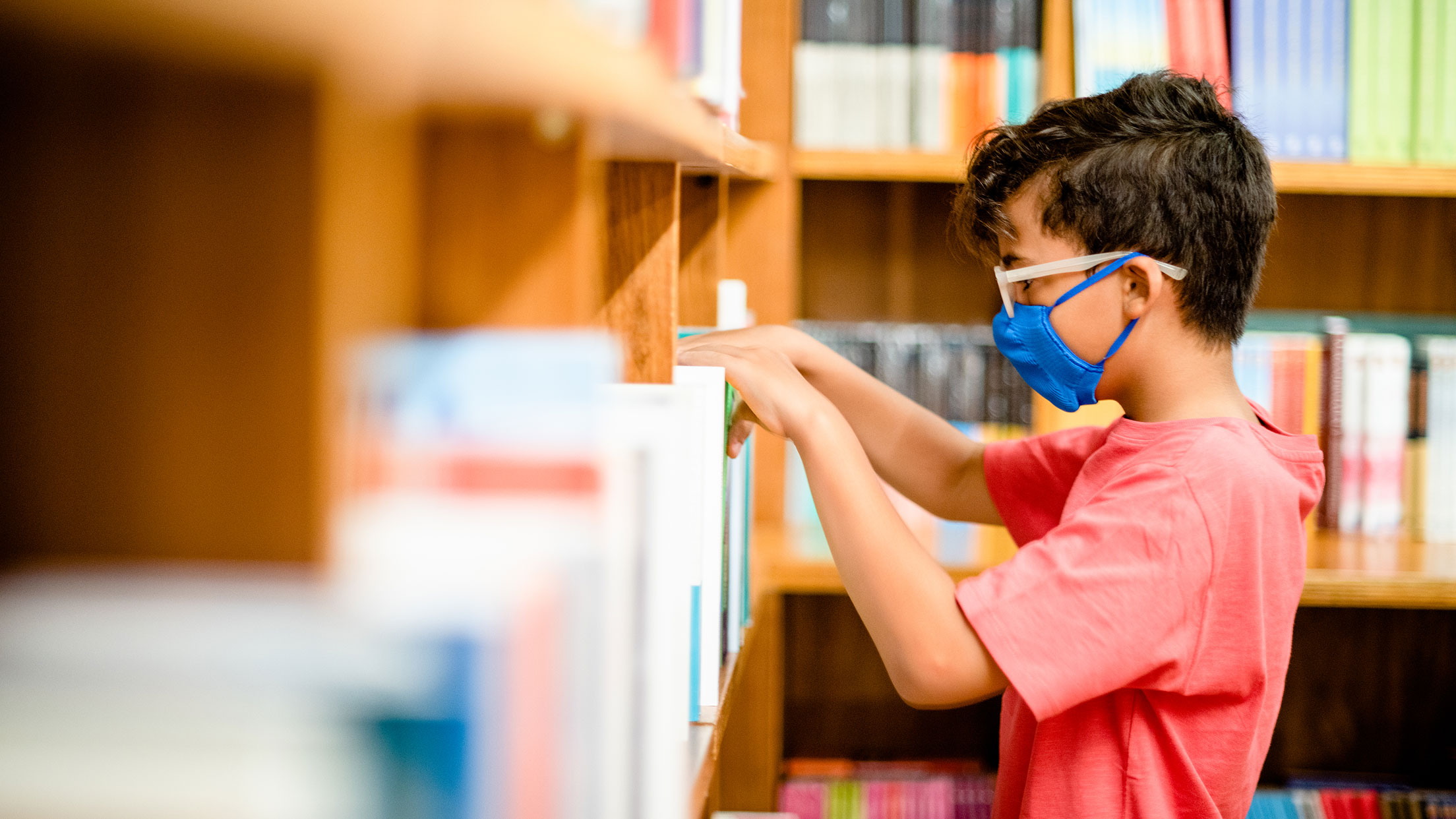 Little boy at library shelf looking at books